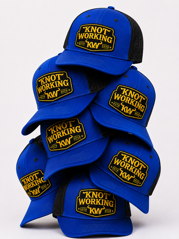 A stack of blue and black trucker hats with a yellow embroidered 'Knot Working' patch on the front, photographed against a clean white background.